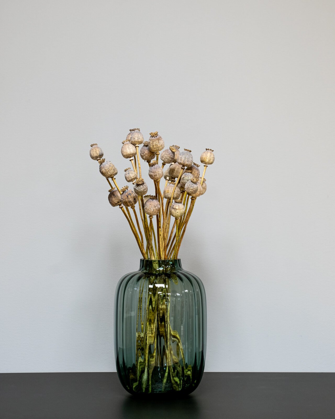 Rustik inredning med torkad vallmo i en stilren keramikvas på en träskänk.